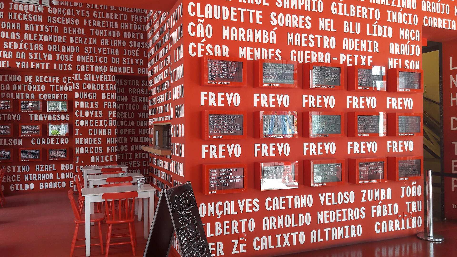 Interior do Paço do Frevo, com paredes vermelhas e a palavra frevo repetida ao lado de nomes de artistas