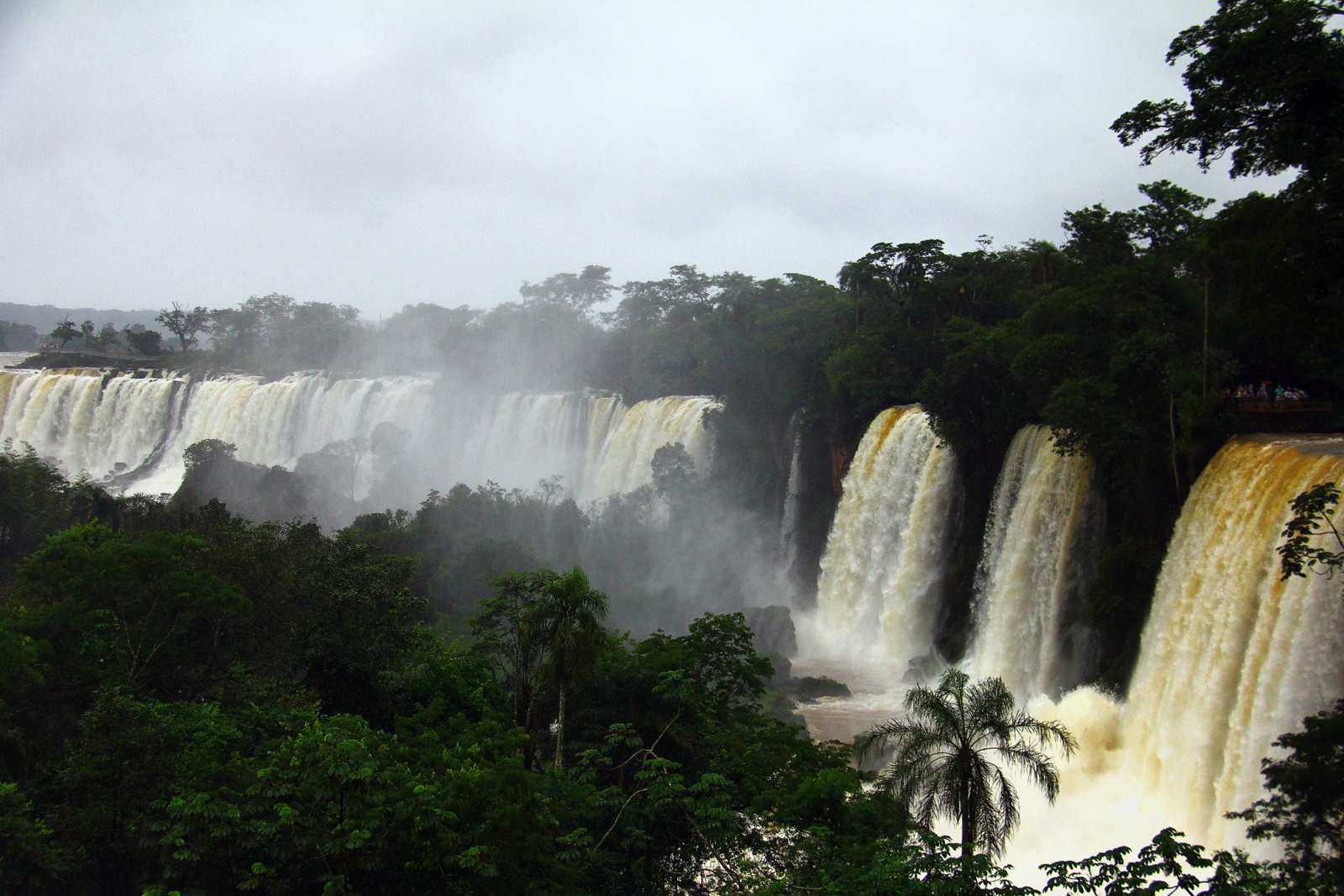 Quedas-d'água do lado argentino das Cataratas, cercadas de mata e névoa, com um mirante ao fundo