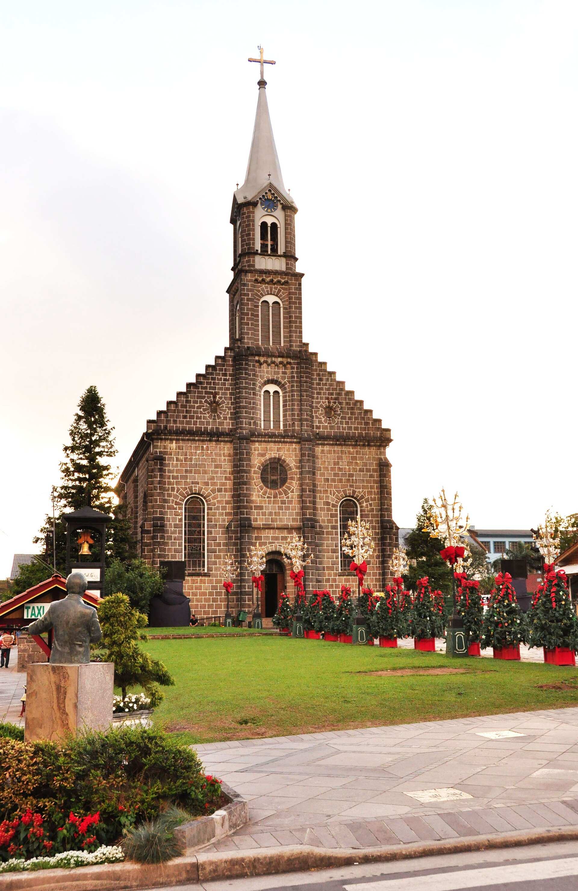 Igreja Matriz São Pedro, de pedra, com torre central, gramado e árvores de Natal em volta, em Gramado