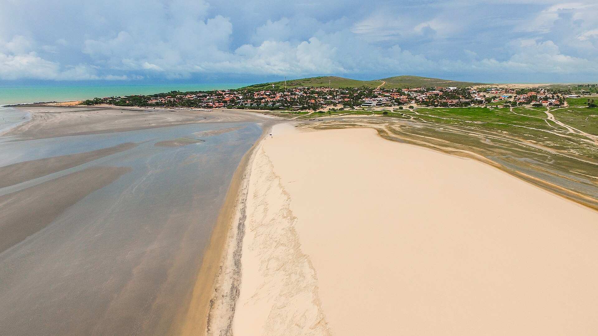 Vista aérea da Duna do Pôr do Sol, com o mar na maré baixa e a vila de Jericoacoara ao fundo