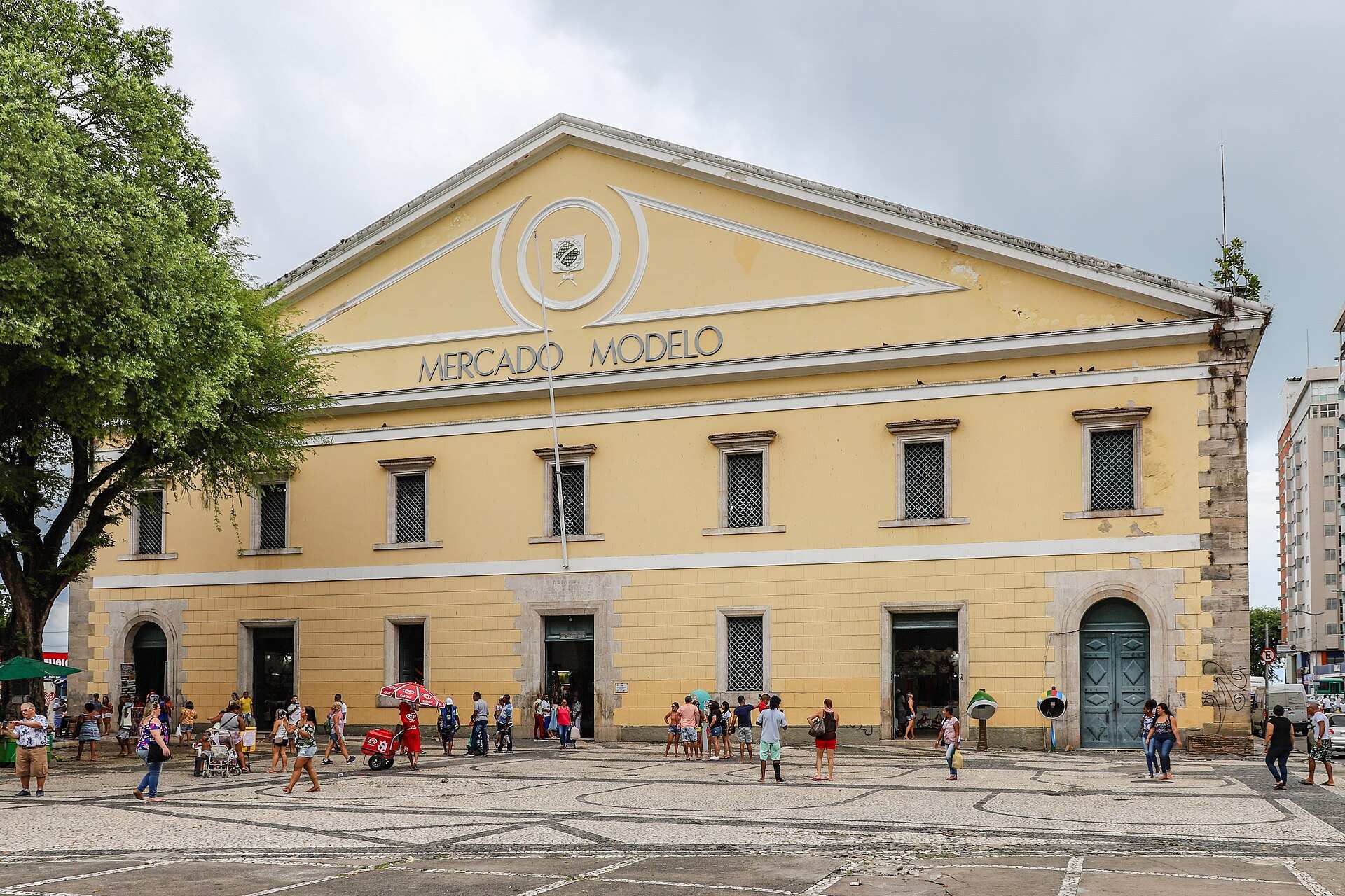 Fachada amarela do Mercado Modelo, na Cidade Baixa de Salvador, com pessoas na praça em frente