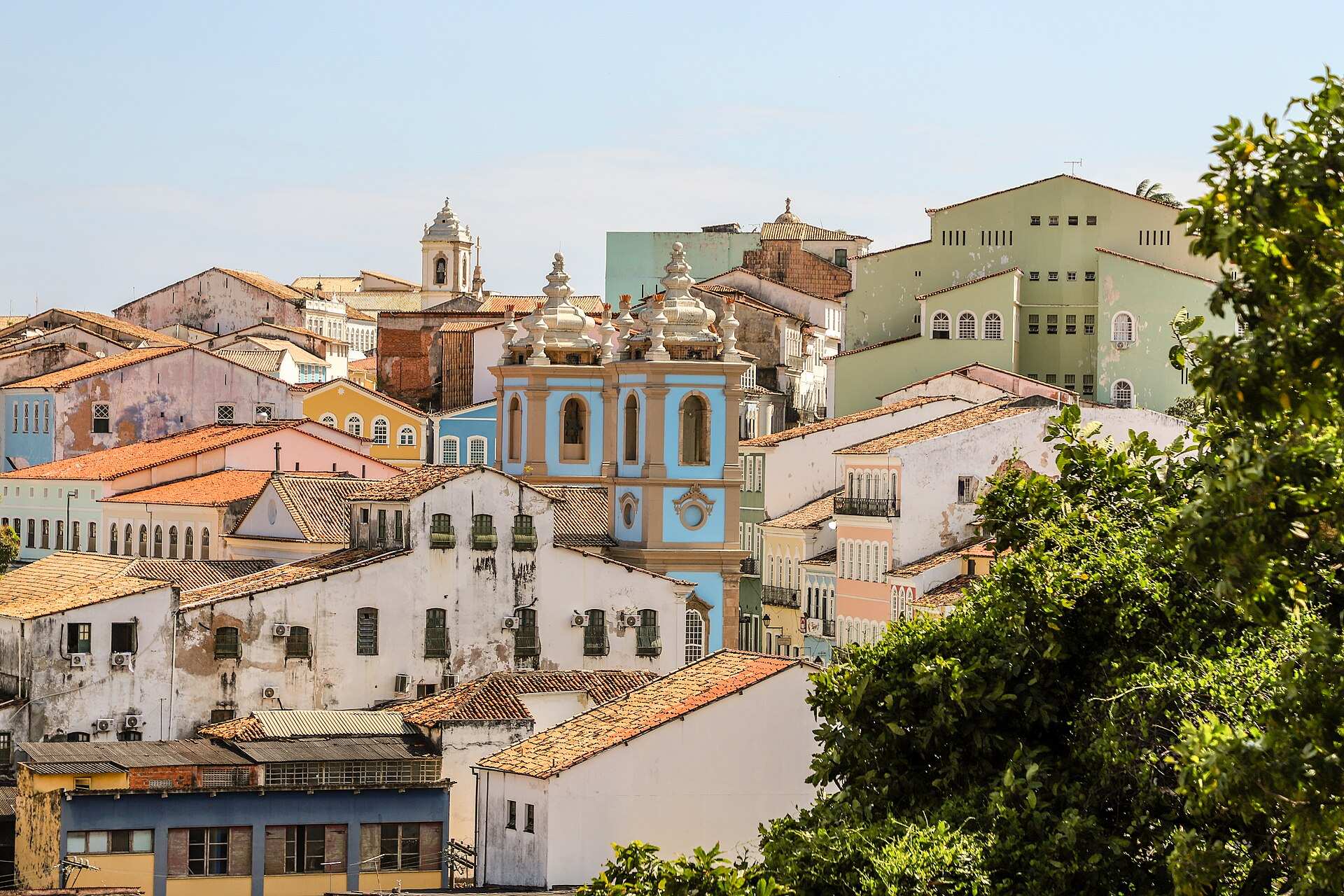 Vista do alto dos telhados e casarões do Pelourinho, com uma igreja barroca de torres azul-claras em destaque