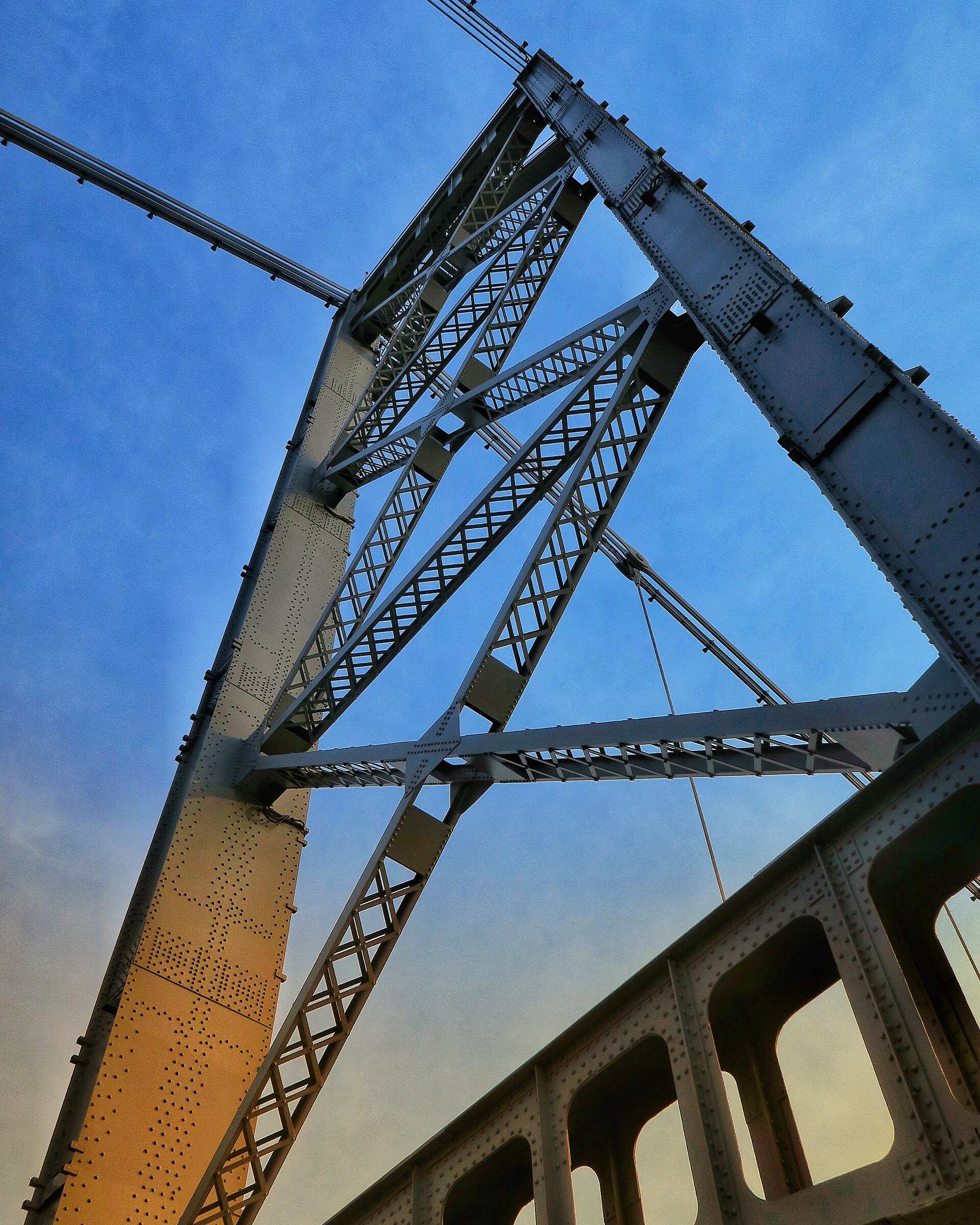 Detalhe da estrutura metálica de uma torre da Ponte Hercílio Luz, vista de baixo, ao entardecer